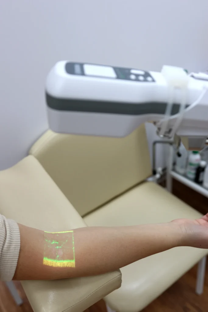Ultrasound therapy device in a clinical setting, demonstrating non-contact treatment with a green mist projected onto a patient's arm for wound care.