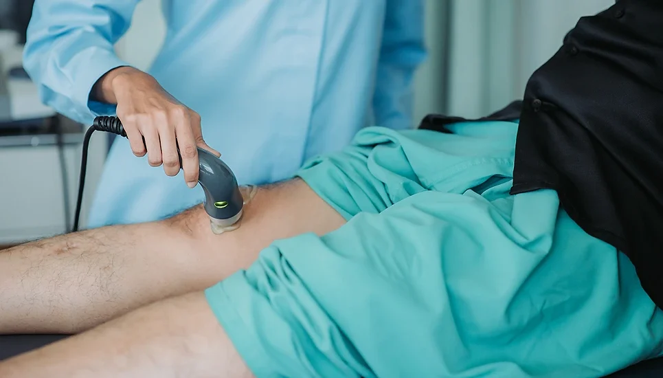 Healthcare professional using ultrasound device on patient's leg for chronic venous insufficiency treatment.